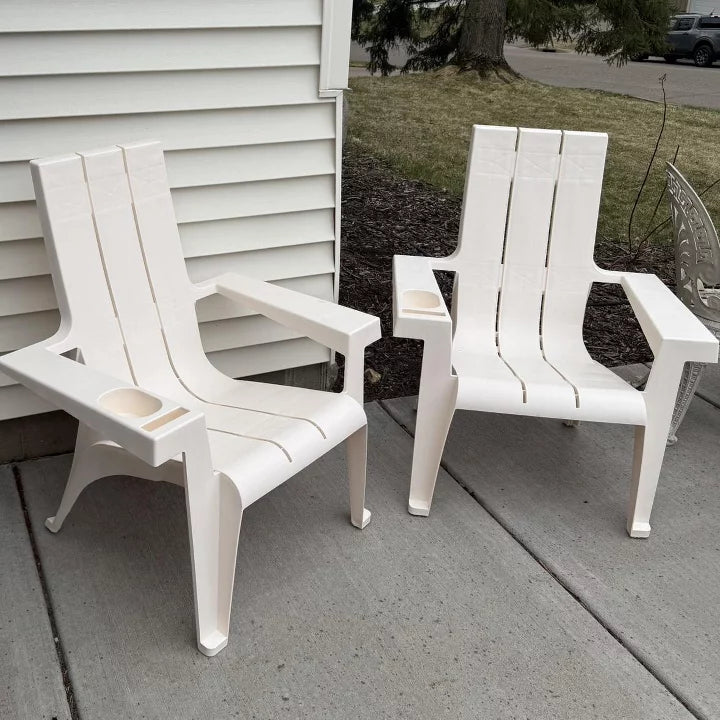 Two white chairs on a concrete patio with a house and grass in the background.